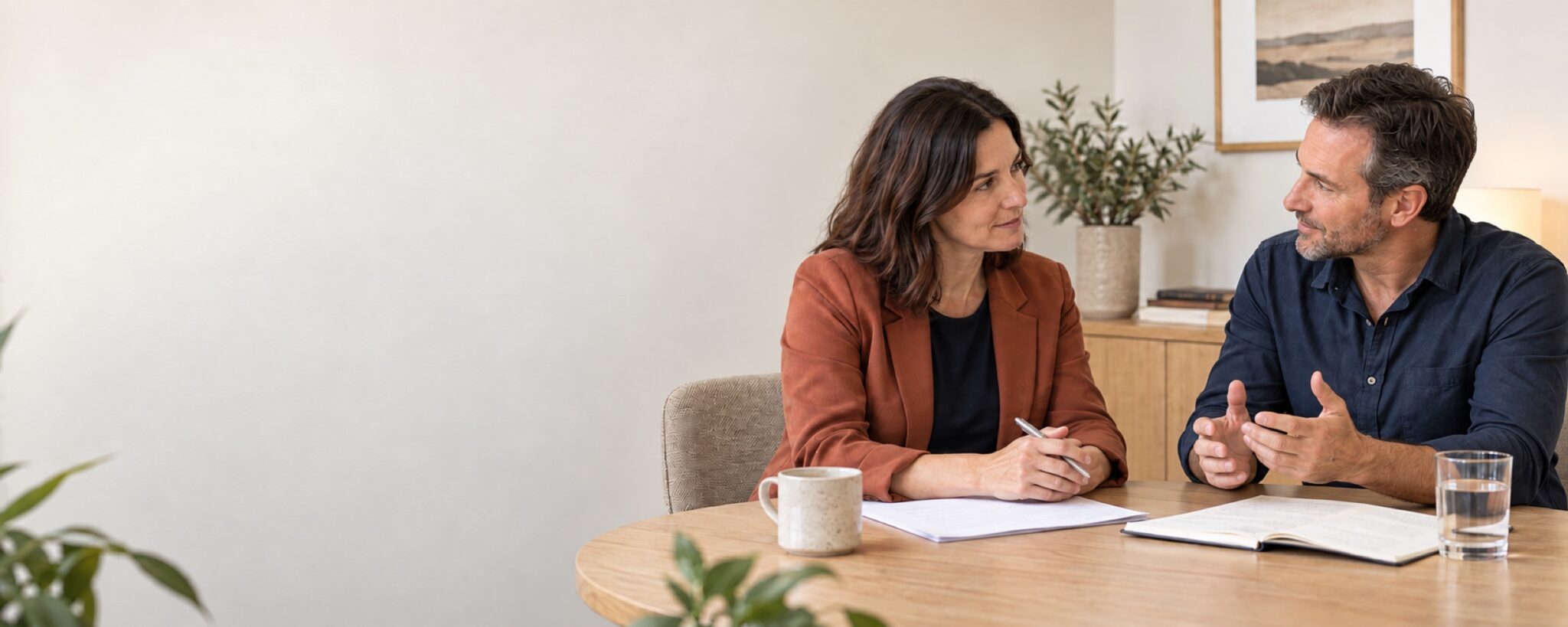 A psychologist and an adult having a respectful conversation at a table with documents in front of them.